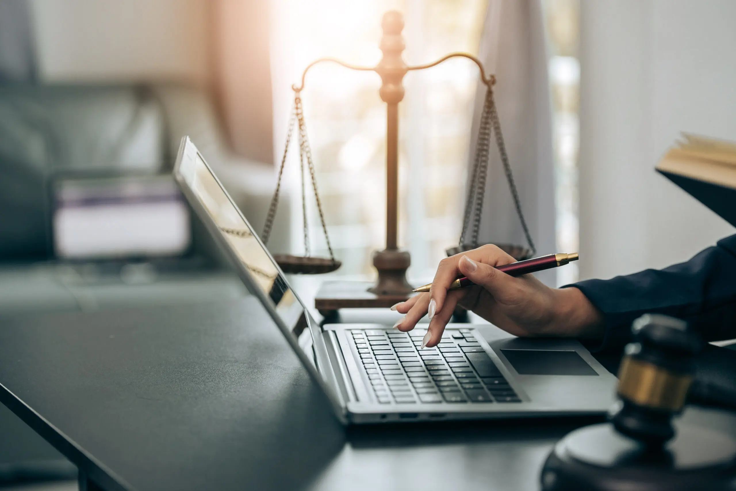 Photo of a woman's hand using a laptop next to the scales of justice